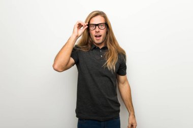 Beyaz duvar gözlüklü ve sürpriz üzerinde uzun saçlı sarışın adam