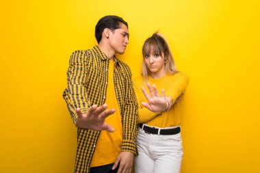 Canlı sarı arka plan üzerinde Genç çift biraz gergin ve ön elleri germe korkuyor
