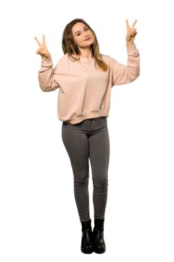 Gülümseyen ve zafer işareti her iki el ile izole beyaz arka plan üzerinde gösterilen pembe kazak bir genç kızla tam uzunlukta bir kadeh