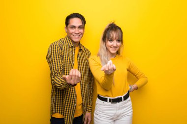 Canlı sarı arka plan üzerinde genç çift el ile gelmeye davet ediyor. Geldiğin için mutluyum.