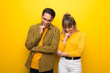 Canlı sarı arka plan üzerinde genç çift çene üzerinde el ile aşağı bakıyor