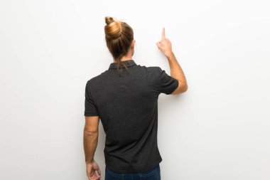 Beyaz duvar geri işaret parmağı ile işaret üzerinde uzun saçlı sarışın adam