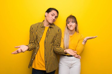 Omuzları kaldırırken önemsiz jest yapan canlı sarı arka plan üzerinde genç çift