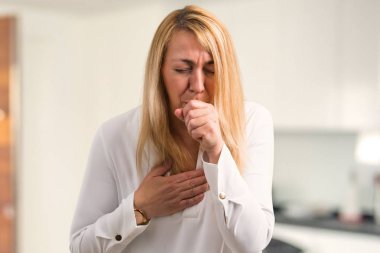 Orta yaş sarışın kadın beyaz gömlek ile öksürük ile acı ve evde kötü hissediyor