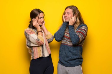 Hippi çift elleriyle kulaklarını kapsayan sarı arka plan üzerinde. Hayal kırıklığı ifade