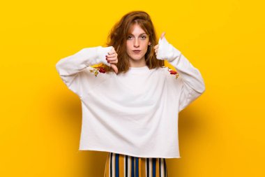 Sarı duvar iyi-kötü işaret yapma genç Kızıl saçlı kadın. Arasında kararsız Evet ya da değil