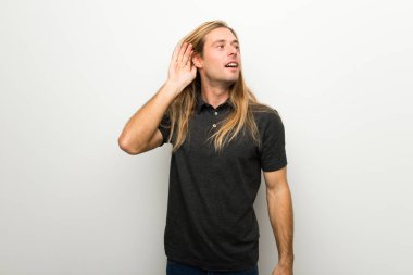 Beyaz duvar için bir şey kulak el koyarak dinleme üzerinde uzun saçlı sarışın adam