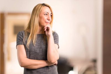 Ayakta ve bir evin içinde yan isteyen gri elbise orta yaş sarışın kadınla