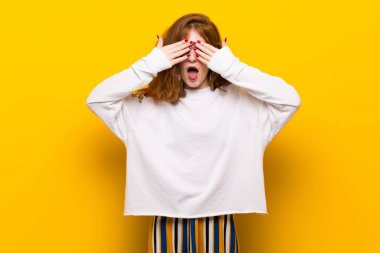 Sarı duvar eller tarafından gözleri kaplama genç Kızıl saçlı kadın. İleride ne olduğunu görmek için sürpriz