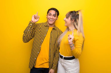 Canlı sarı arka plan üzerinde genç çift bir parmak kaldırırken çözüm gerçekleştirmek niyetinde