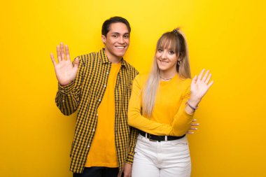 Canlı sarı arka plan üzerinde genç çift mutlu ifade ile el ile selamlama