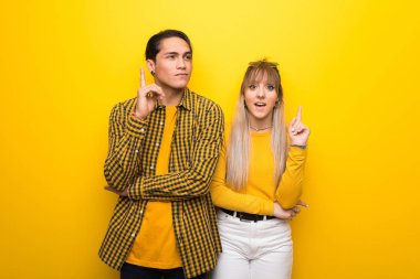 Canlı sarı arka plan üzerinde genç çift bir fikir parmak işaret düşünme