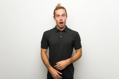 Sürpriz ve şok yüz ifadesi ile beyaz duvarın üzerinden uzun saçlı sarışın adam