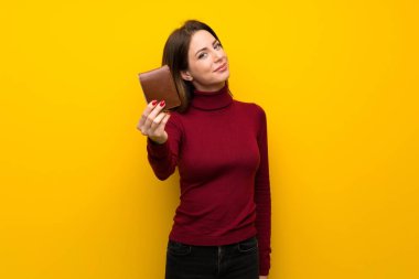 Balıkçı yaka bir cüzdan tutan sarı duvarın üzerinden kadınla