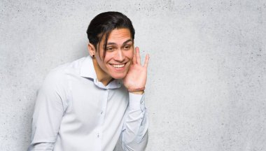 Yakışıklı adam dokulu duvar arka plan üzerinde kulak elini koyarak bir şey dinlerken