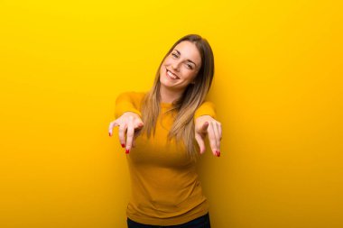 Süre gülümseyen genç kadın sarı arka plan üzerinde parmak seni işaret