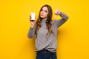 Genç kadın sorunlu holding smartphone kırık ile sarı duvarın üzerinden
