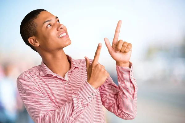 Young african american man pointing with the index finger a great idea and looking up on unfocused outdoor background