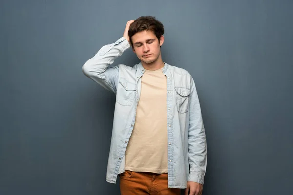 Teenager man with jean jacket over grey wall with an expression of frustration and not understanding
