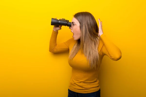 Mujer Joven Sobre Fondo Amarillo Mirando Lejos Con Prismáticos — Foto de Stock