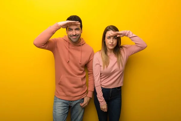 Group of two people on yellow background looking far away with hand to look something