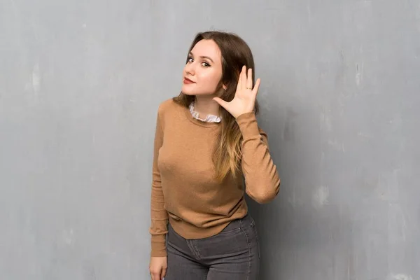 耳に手を置くことによって何かを聞いて織り目加工の壁を越えてティーンエイ ジャーの女の子 — ストック写真