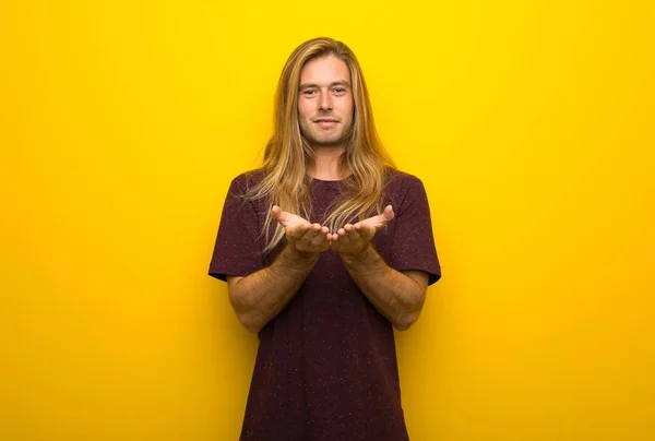 広告を挿入する手のひらに架空 Copyspace を保持している黄色の壁に長い髪の金髪の男 — ストック写真