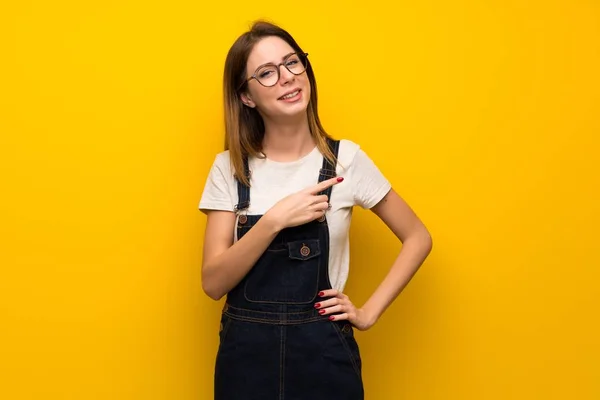 Woman over yellow wall pointing to the side to present a product