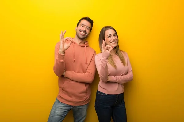 Group of two people on yellow background showing an ok sign with fingers