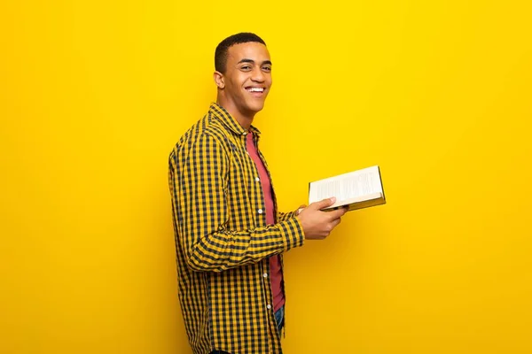 Junger Afroamerikanischer Mann Auf Gelbem Hintergrund Hält Ein Buch Der — Stockfoto