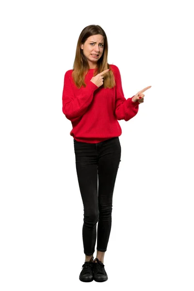 一个穿着红色毛衣的年轻女子的全长照片吓得指着被孤立的白色背景的一侧 — 图库照片