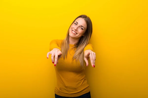 黄色背景に若い女性が笑顔で指をポイントします — ストック写真