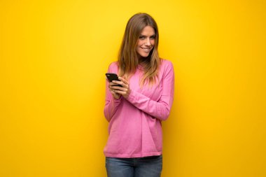 Mobil ileti gönderme sarı duvarın üzerinden pembe kazaklı kadın