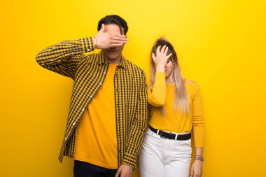 Canlı sarı arka plan üzerinde genç çift elleri ile gözleri kaplayan. Bir şey görmek istemiyorum