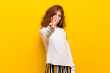 Sarı duvar mutlu ve sayım üç parmak ile genç Kızıl saçlı kadın