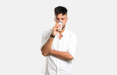 Beyaz gömlekli Arap genç bir adam, elinde gri arka plandaki paket kâğıt bardakta sıcak kahve tutuyor.