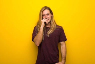 Tatlı bir ifadeyle gülümseyen sarı duvarın üzerinden uzun saçlı sarışın adam