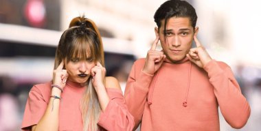 Şehirde elleri ile iki kulaklarını kapatan genç çift