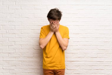 Genç adam yorgun ve hasta ifade ile beyaz tuğla duvarın üzerinden