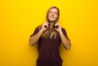 Kulaklıklar ile sarı duvarın üzerinden uzun saçlı sarışın adam
