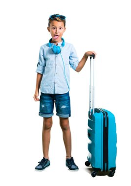 Çocuk tam vücut güneş gözlüğü ve kulaklık bavulunu komik göz izole beyaz arka plan üzerinde olan kamera Dil Gösterilen ile seyahat ile