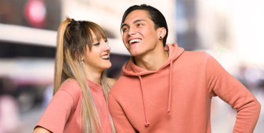 Genç çift kalça kolları ile poz ve şehirde gülüyor