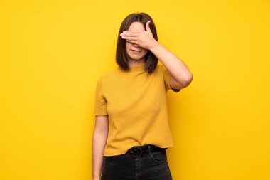 Sarı duvar eller tarafından gözleri kaplama genç kadın. Bir şey görmek istiyor musunuz