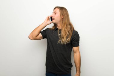 Cep telefonu ile bir konuşma tutmak beyaz duvarın üzerinden uzun saçlı sarışın adam