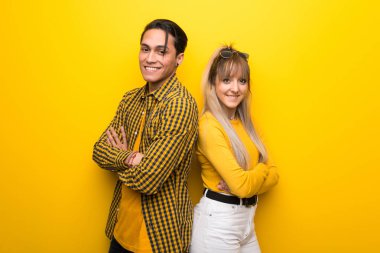 Canlı sarı arka plan üzerinde genç çift gülümseyerek kollarını yanal pozisyonda geçti tutmak