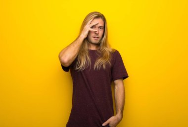 Sürpriz ve şok yüz ifadesi ile sarı duvarın üzerinden uzun saçlı sarışın adam