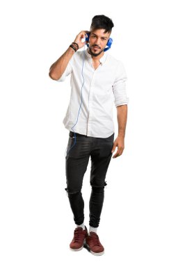 Beyaz gömlekli, kulaklıklı, izole edilmiş beyaz arka planda müzik dinleyen Arap bir gencin tam boy fotoğrafı.