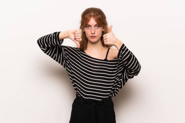 Beyaz duvar iyi-kötü işaret yapma genç Kızıl saçlı kadın. Arasında kararsız Evet ya da değil