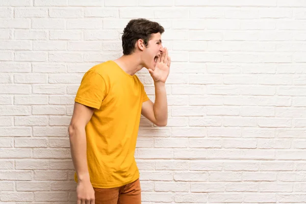 Genç Adam Için Lateral Açık Ağızlı Bağırmayı Beyaz Tuğla Duvarın — Stok fotoğraf