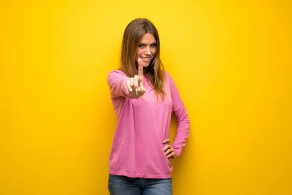 黄色の壁を示すと 指を持ち上げる上のピンクのセーターの女性 — ストック写真